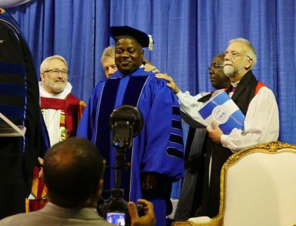 Man wearing blue academic robes surrounded by four people in clerical garb